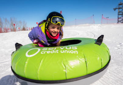 Girl smiling on a tube at the Servus Tube Park located in Calgary on a snowy hill