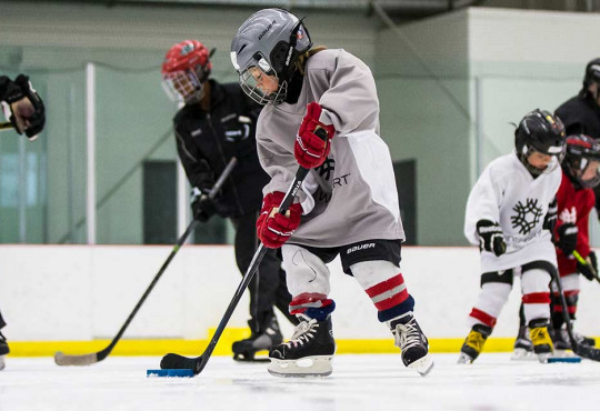 Young boy learning how to play hockey while carrying a puck