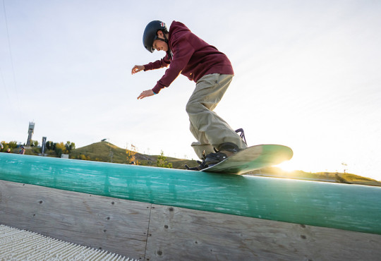 Young freestyler sliding down WinSports DrySlope rail on their snowboard