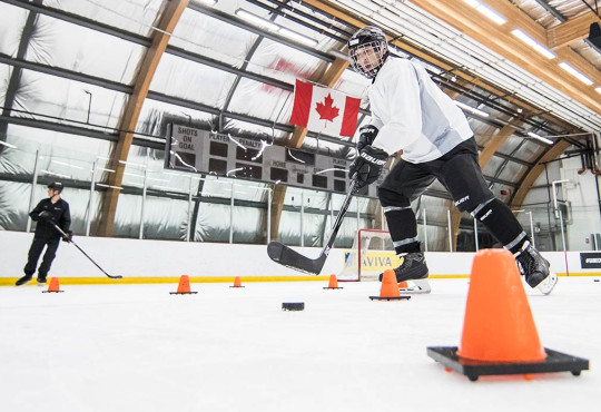 Adult learning how to stick handle through pylons at a hockey lesson at WinSport