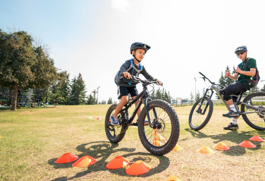 Young biker learning the basics of mountain bike with an instructor watching