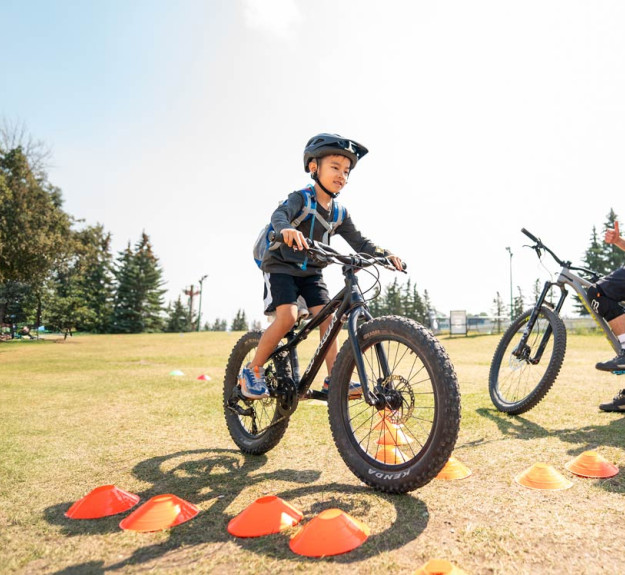 Young biker learning the basics of mountain bike with an instructor watching