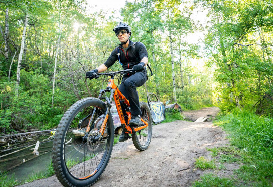Adult male riding bike through a trail covered by trees at WinSport