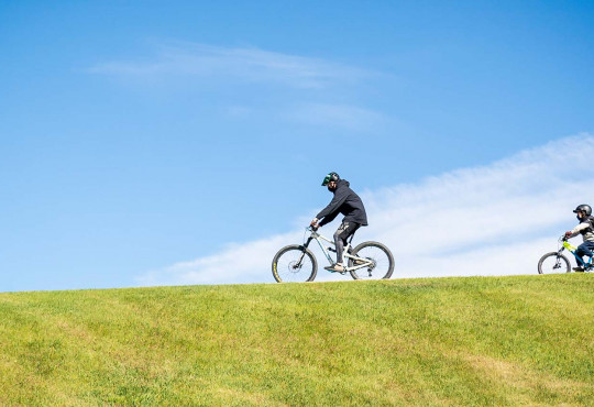 Instructor and boy riding mountain bikes across a grassy hill