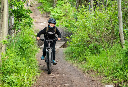 Young boy exiting a tree covered trail on his bicycle