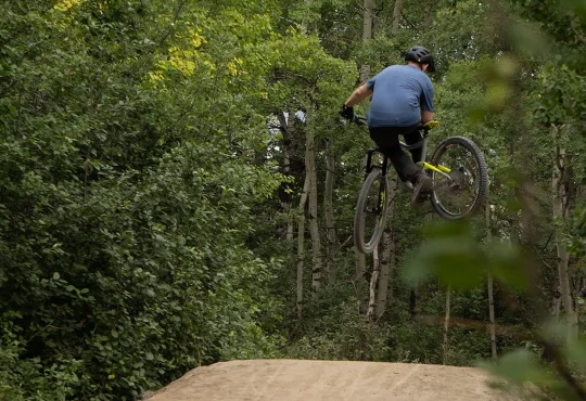 Mountain biker going off a dirt jump on a WinSport mountain bike trail