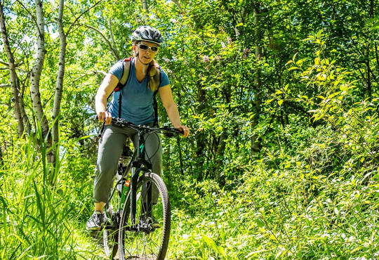 Woman on bicycle riding through the tree at WinSport during a mountain bike lesson