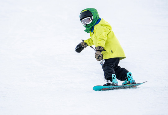 Small child snowboarding on toe edge down snow hill at winsport