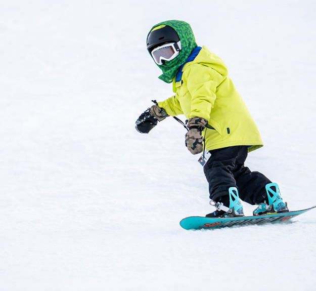 Small child snowboarding on toe edge down snow hill at winsport