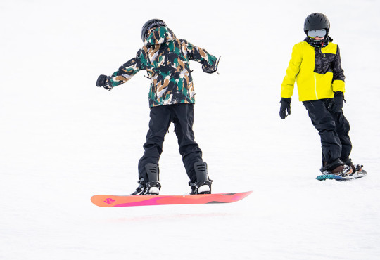 Two teenage boys snowboarding close together down the hill at winsport
