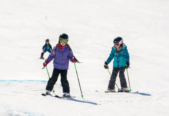 Two first time skiiers learning how to ski down the WinSport hil