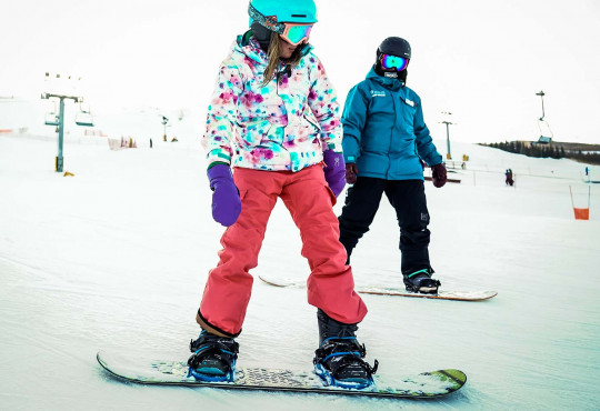 Female learning how to snowboard with instructor