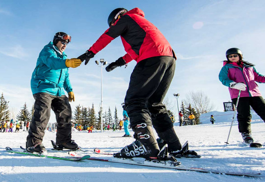 Private lesson instructor teaching new skiiers how to stand on snow at winsport copy