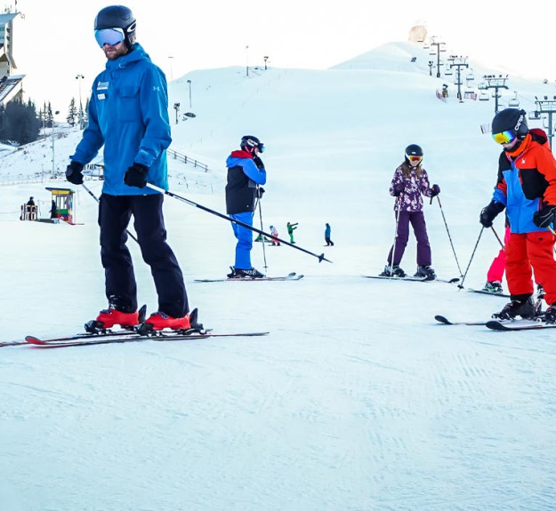 Ski instructor leading a group of children down the hill during a ski lesson in winter