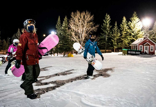 Three women walking with their snowboards up the bunny hill