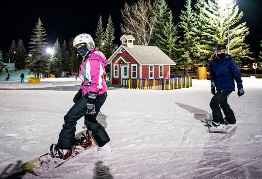 Two women learning to snowboard at night at WinSport
