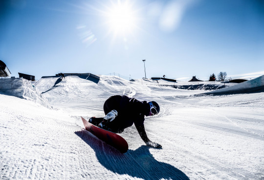 WinSport Snowboard intermediate snowboarder carves a turn and touches the snow with one hand