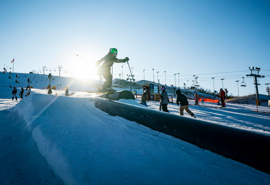 Skier hitting a rail at the terrain park at WinSport on opening day