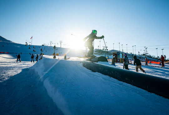 Ski Fundamentals Skier hitting a rail at the terrain park at WinSport on opening day