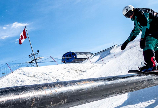 adult riding their snowboard on a rail down the alpine hill at winsport v2