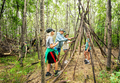 Group of campers learning how to built a wilderness shelter out of sticks v2