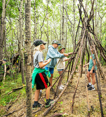 Group of campers learning how to built a wilderness shelter out of sticks v2