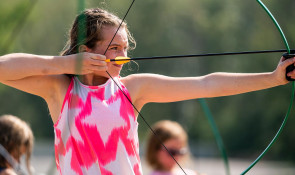 Girl aiming a bow and arrow while at Wilderness summer camp at WinSport