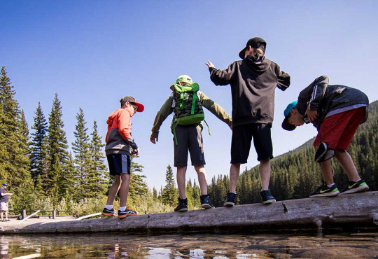 Group of children walking over a tree stump on a shallow river