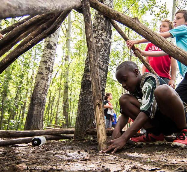 Group of young children learning how to build shelter in the wilderness at a WinSport summer camp