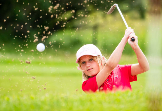 Child swinging a golf club in a bunker on the golf course during a Rinks and Links program at WinSport