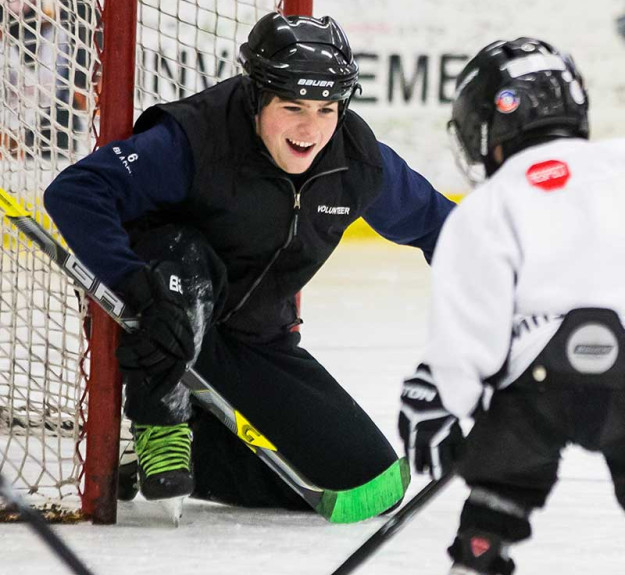 WinSport volunteer playing goalie against small hockey player